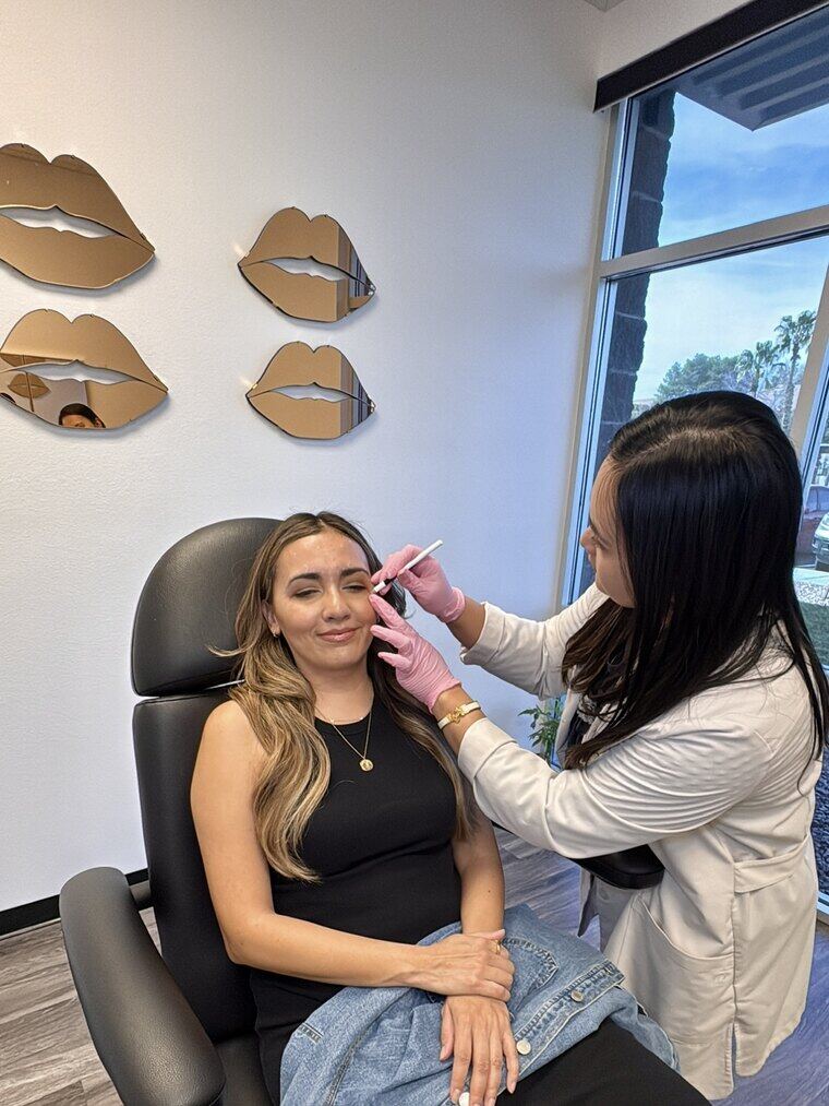 A client reclined in the treatment chair receiving an injectable treatment, with the studio's lip-shaped wall mirrors behind her.