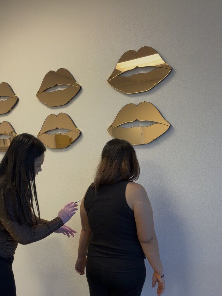 Bianca preparing an arm injection for a client beside the studio's lip-shaped wall mirrors.